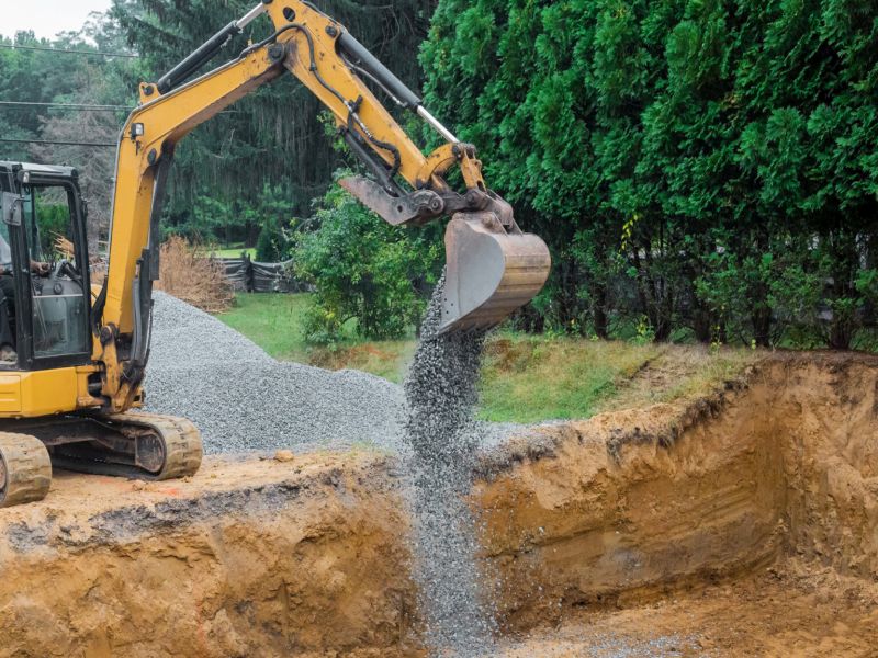 A yellow excavator bucket shovel moving gravel stones of foundation on a construction site stone backfill